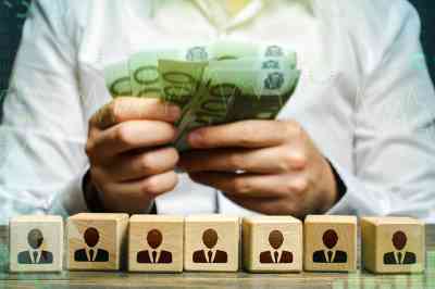 © Andrii Yalanskyi - Adobe Stock.com Figuren auf Würfeln und Hände mit Geldscheinen