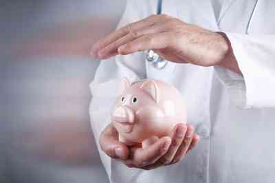 © andranik123 - stock.adobe.com Arzt hält Hand über Sparschwein