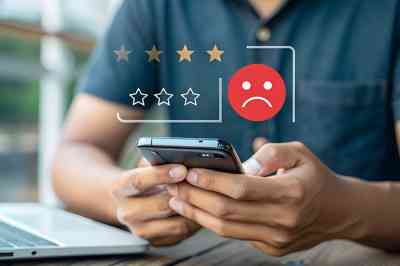 © main_asn - stock.adobe.com Mann bedient Smartphone, darüber negatives Smiley und schlechte Sterne Bewertung